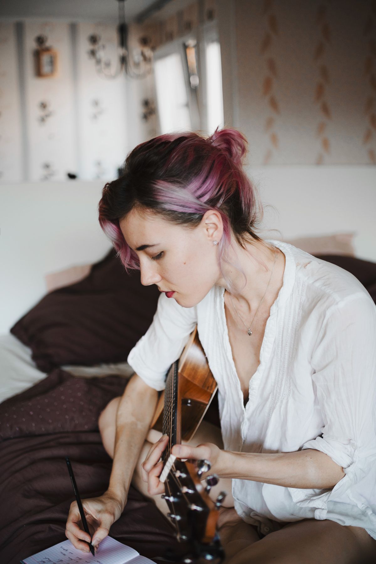 Linn writing in a notebook with a guitar across her lap